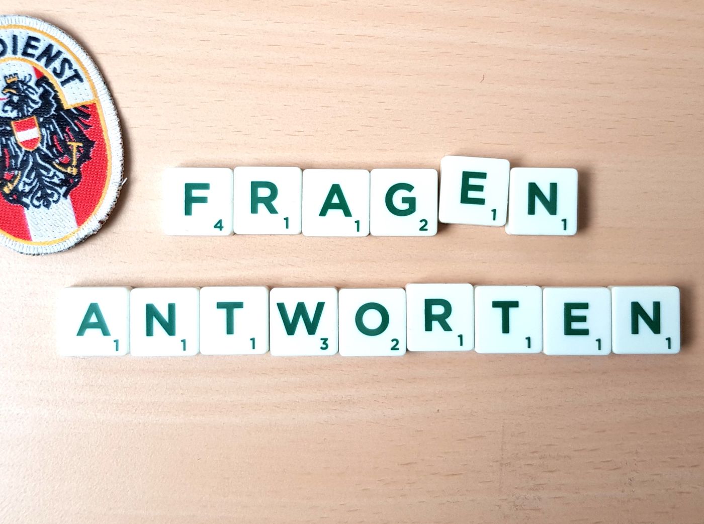 Kleine Spielzeugplättchen mit den aufgedruckten Großbuchstaben „Fragen“ und „Antworten“, am linken oberen Bildschirmrand ist das Zivildienstabzeichen zu sehen.
